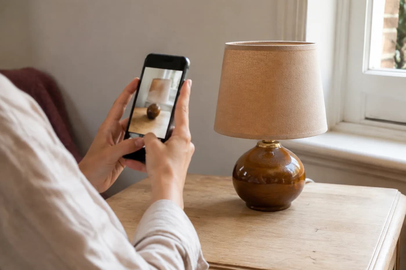 Une personne photographie une lampe près d’une fenêtre.